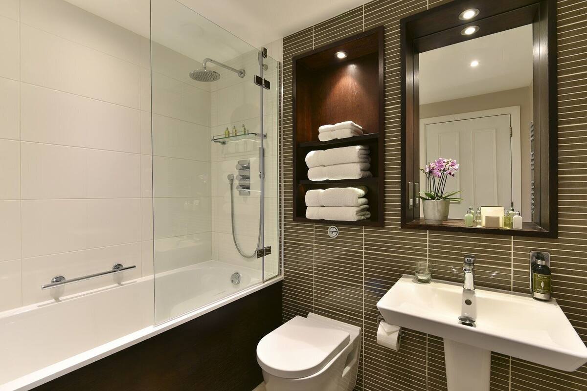 Une salle de bain moderne avec une douche à parois de verre, un lavabo blanc et des toilettes. On y trouve des étagères avec des serviettes pliées et un miroir au-dessus du lavabo.