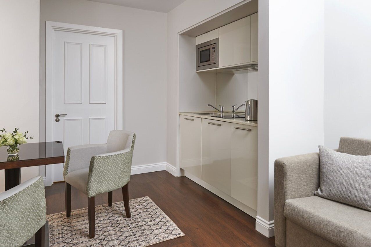 A compact kitchen with a microwave, sink, and cabinets. There is a dining table with chairs and a sofa in the living area.