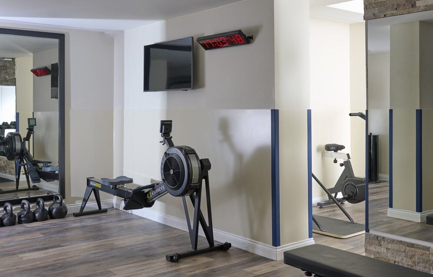A home gym with a rowing machine, dumbbells, an exercise bike, and a TV mounted on the wall.