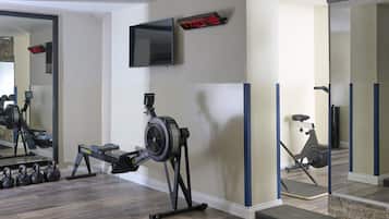 Ein Heimfitnessraum mit Rudergerät, Hanteln, Ergometer und einem an der Wand befestigten Fernseher.