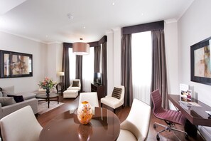 A modern hotel room with a round dining table, a comfortable sofa, a swivel office chair, and a television. - Fraser Suites Queens Gate (London)
