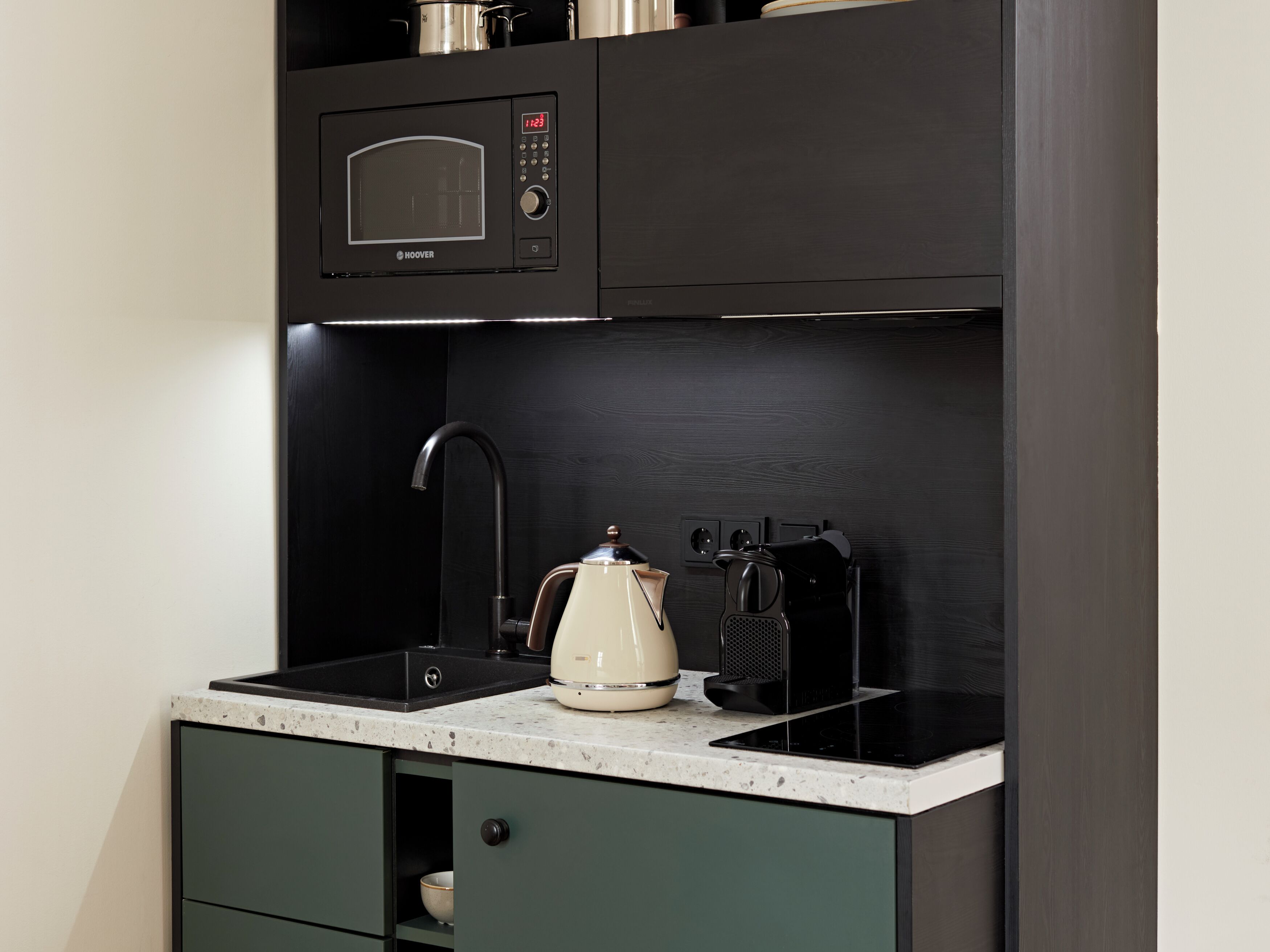 A compact kitchen with a built-in microwave, a kettle, and a coffee maker on the countertop.