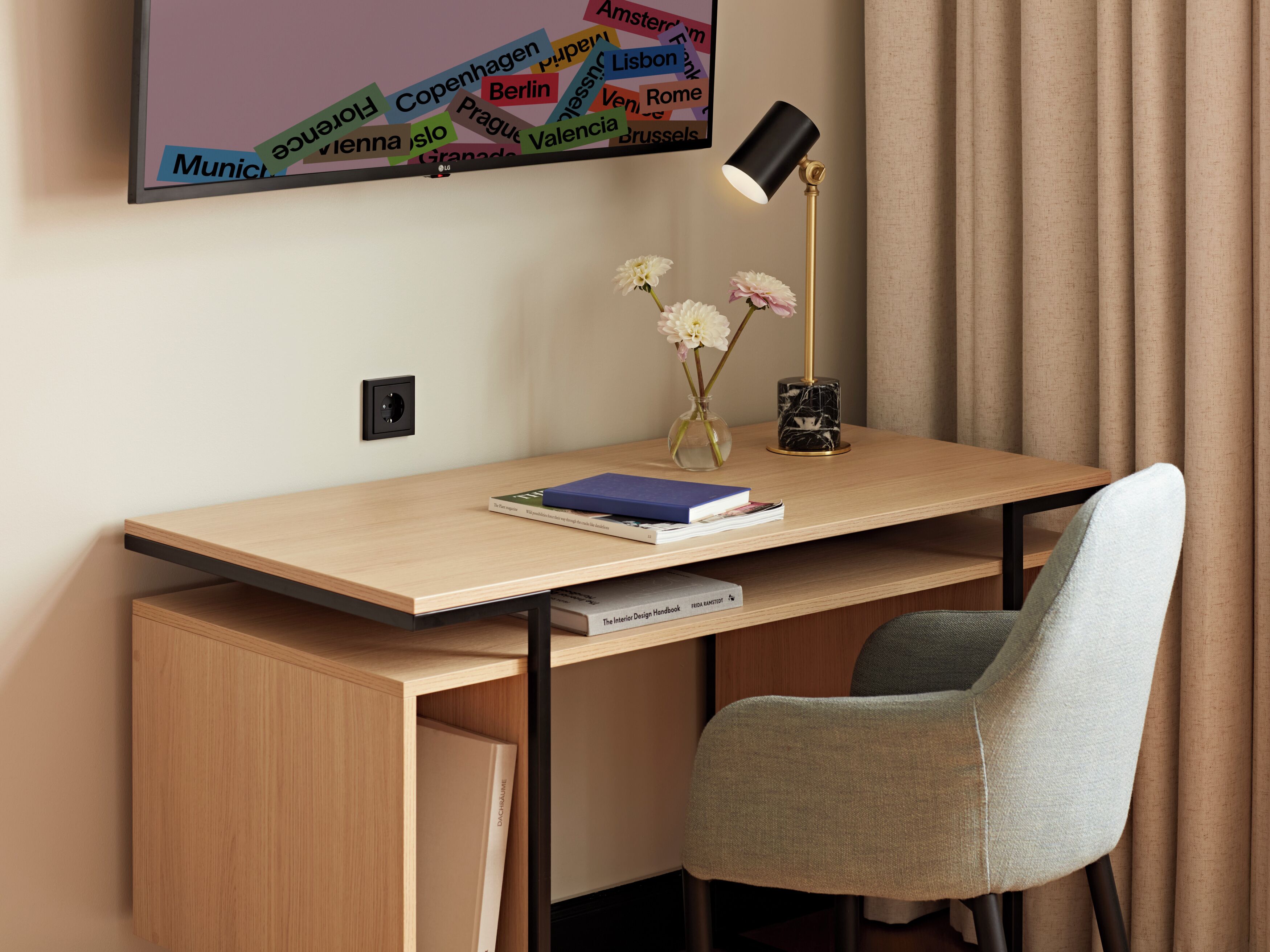 Un escritorio moderno con una lámpara, una silla y un televisor de pared que muestra nombres de ciudades.