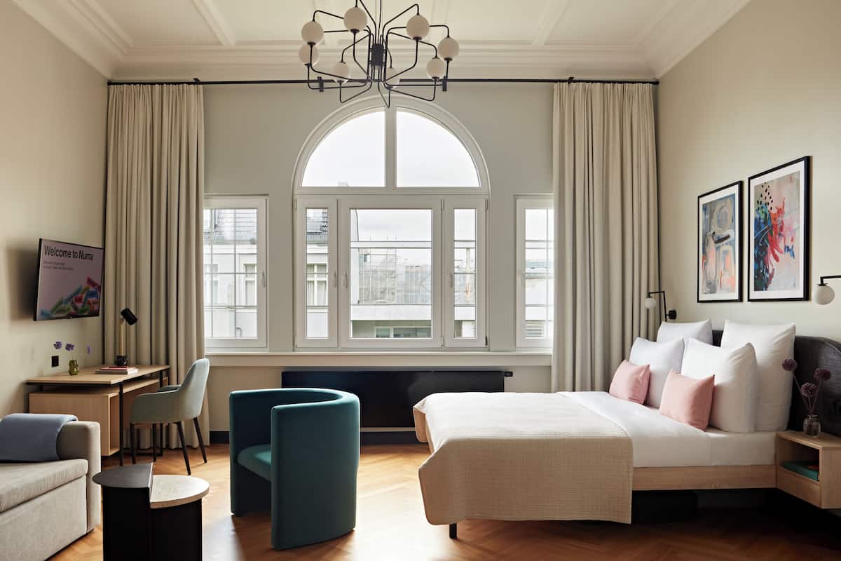 Een moderne slaapkamer met een groot bed, een bureau, een stoel en een stadszicht door grote ramen.