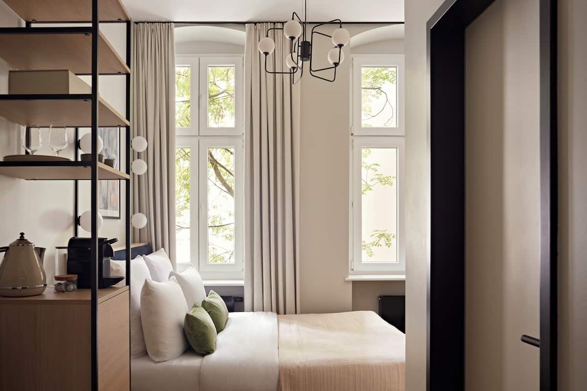 Een slaapkamer met een bed, een plank met keukengerei en een raam met gordijnen.