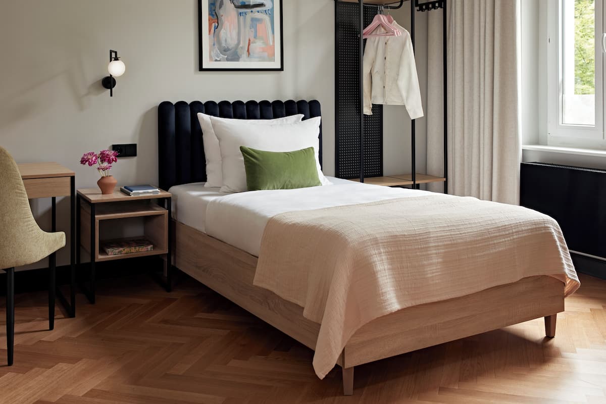 Een keurig opgemaakt slaapkamer met een bed, nachtkastjes, een stoel, een kledingrek en een schilderij aan de muur.