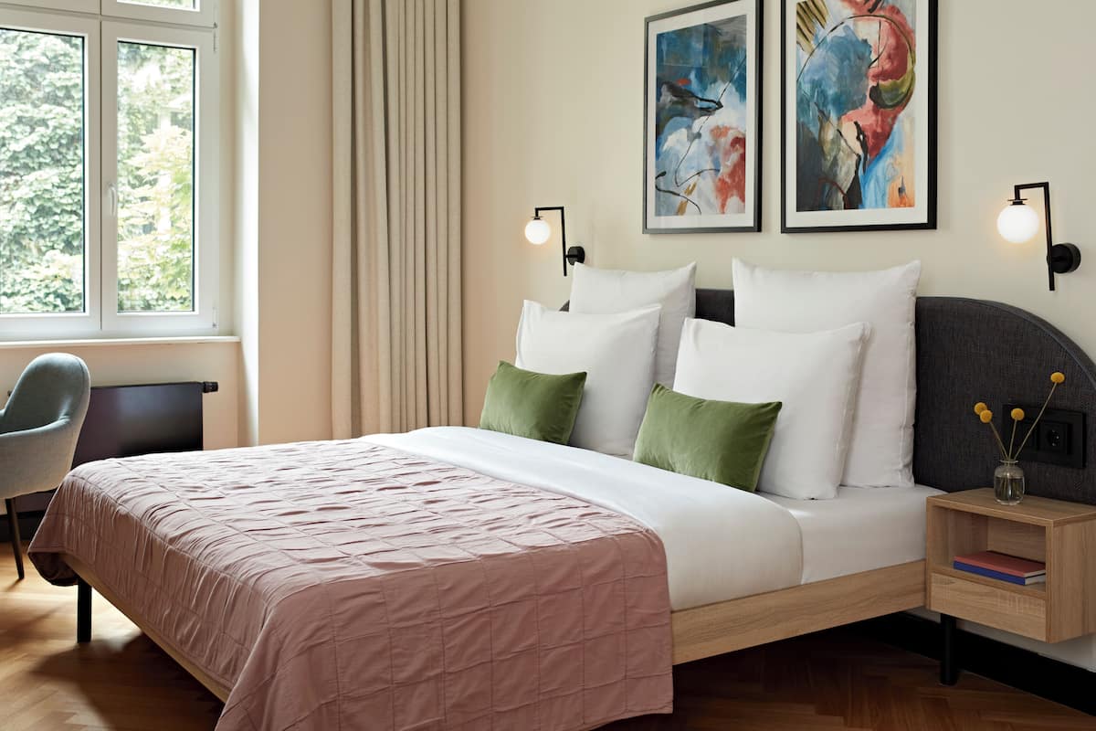 Een netjes opgemaakte slaapkamer met een bed, nachtkastjes, een stoel en kunst aan de muur.