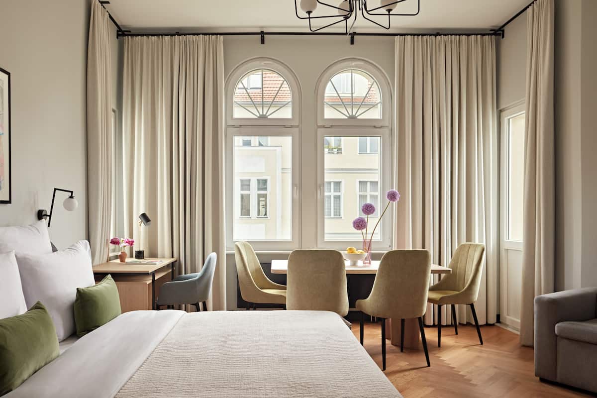 Een moderne hotelkamer met een groot bed, een zithoek met stoelen, een tafel en een uitzicht door grote ramen.