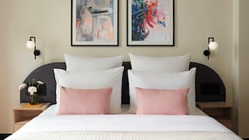 A hotel room with a large bed, two wall-mounted paintings, bedside lamps, and a nightstand with a vase of flowers.