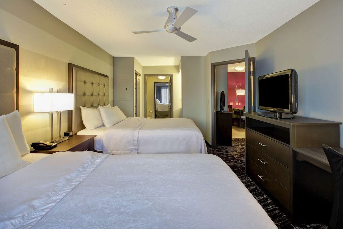 A hotel room with two beds, a desk, a television, and a ceiling fan.
