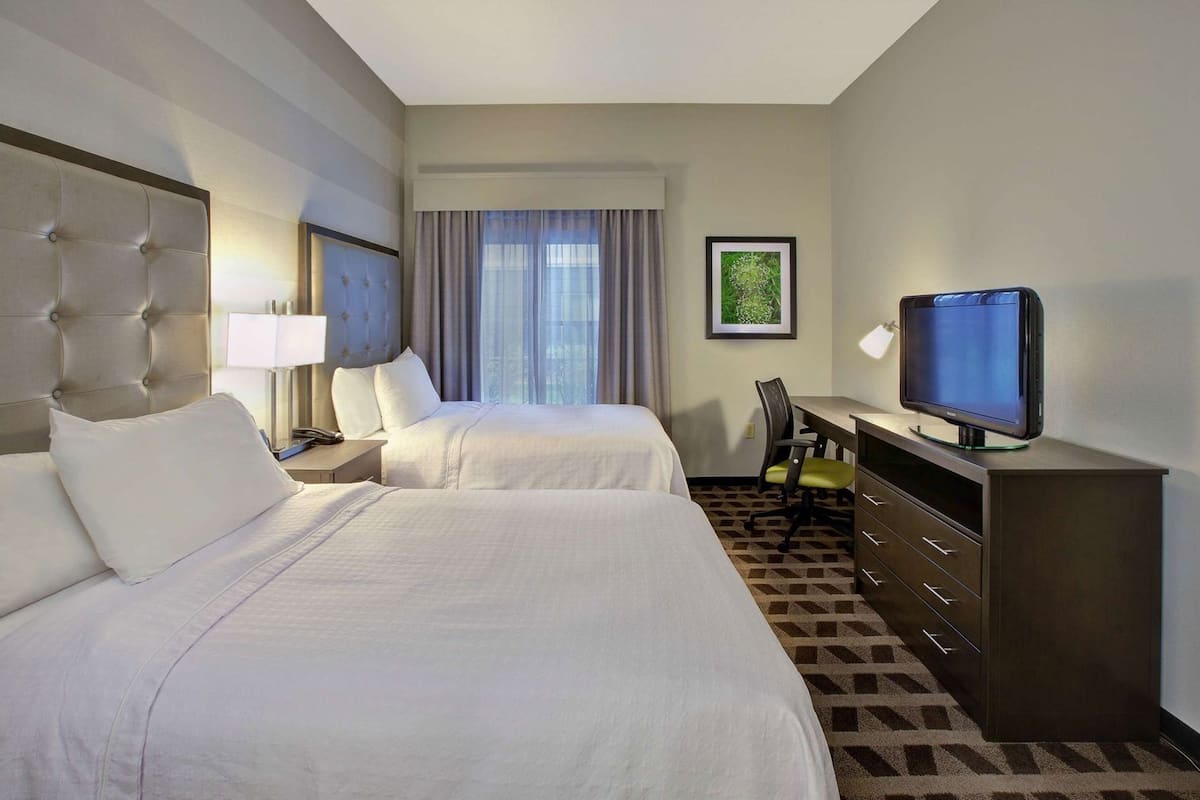 A hotel room with two beds, a desk with a television, a chair, and a framed picture on the wall.