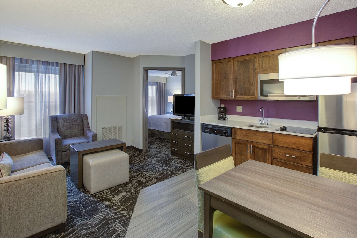 A hotel room with a living area, kitchenette, and a bed.