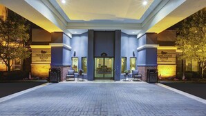 A hotel entrance with a modern design, featuring a prominent entrance, a clear sign reading "Homewood Suites Hilton," and a well-lit pathway leading to the entrance.
