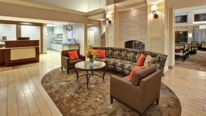 A spacious lobby with a reception desk, a seating area with a sofa and armchairs, a coffee table with flowers, and a fireplace.