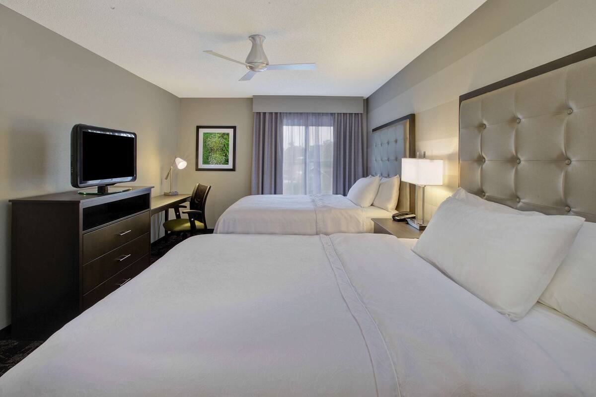 A hotel room with two beds, a television, a desk, and a chair.