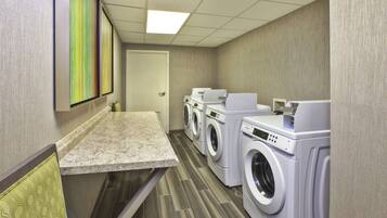 A hotel laundry room with a row of washers and dryers, a countertop, and a door.