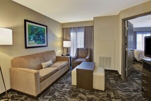 Habitación de hotel con sofá, sillón, mesita de centro y un cuadro en la pared.