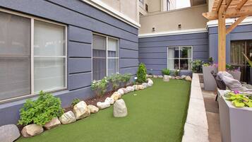 Un patio con césped artificial, un sendero bordeado de rocas y plantas en macetas.
