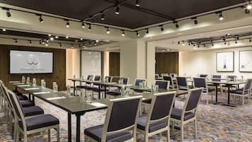 A conference room with long tables, chairs, and a projection screen displaying 'The Windsor Suites'.