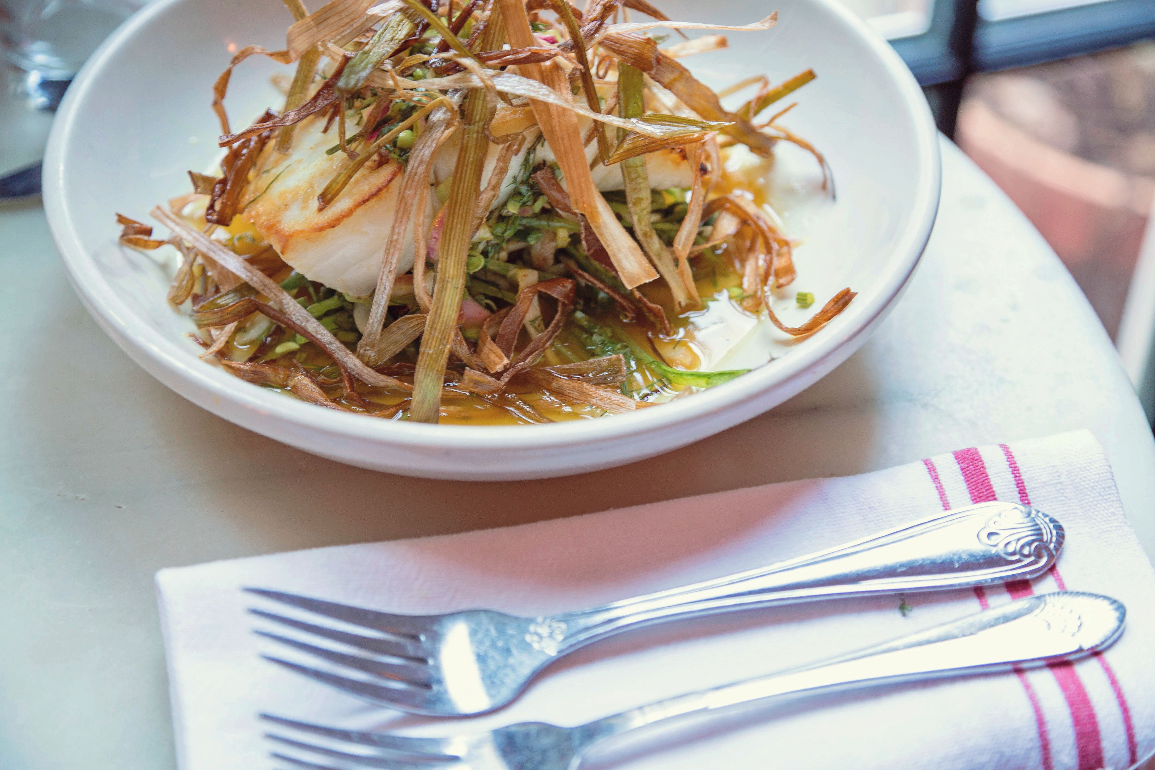 A white bowl of food with a fork and napkin on a table.