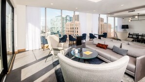 Una habitación de hotel moderna con un ventanal grande, un sofá, sillas, una mesa de centro y un comedor.