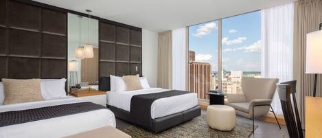 A hotel room with two beds, a large window with a city view, a seating area, and a modern design.