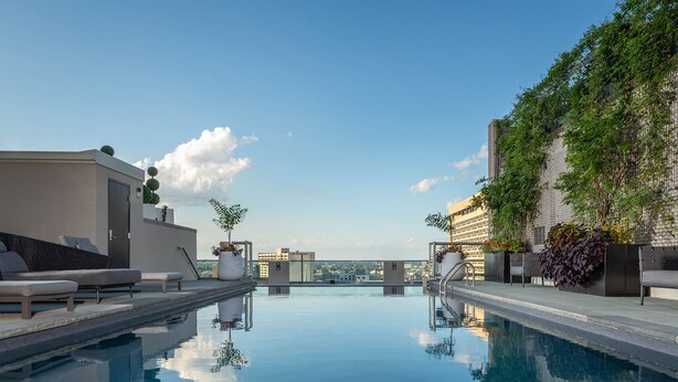 Una piscina infinita en la azotea con sillones, plantas en macetas y vistas de la ciudad.