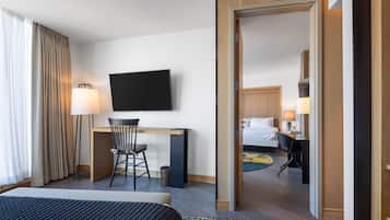 A hotel room with a bed, a desk with a chair, a television, and a bathroom visible through an open door.