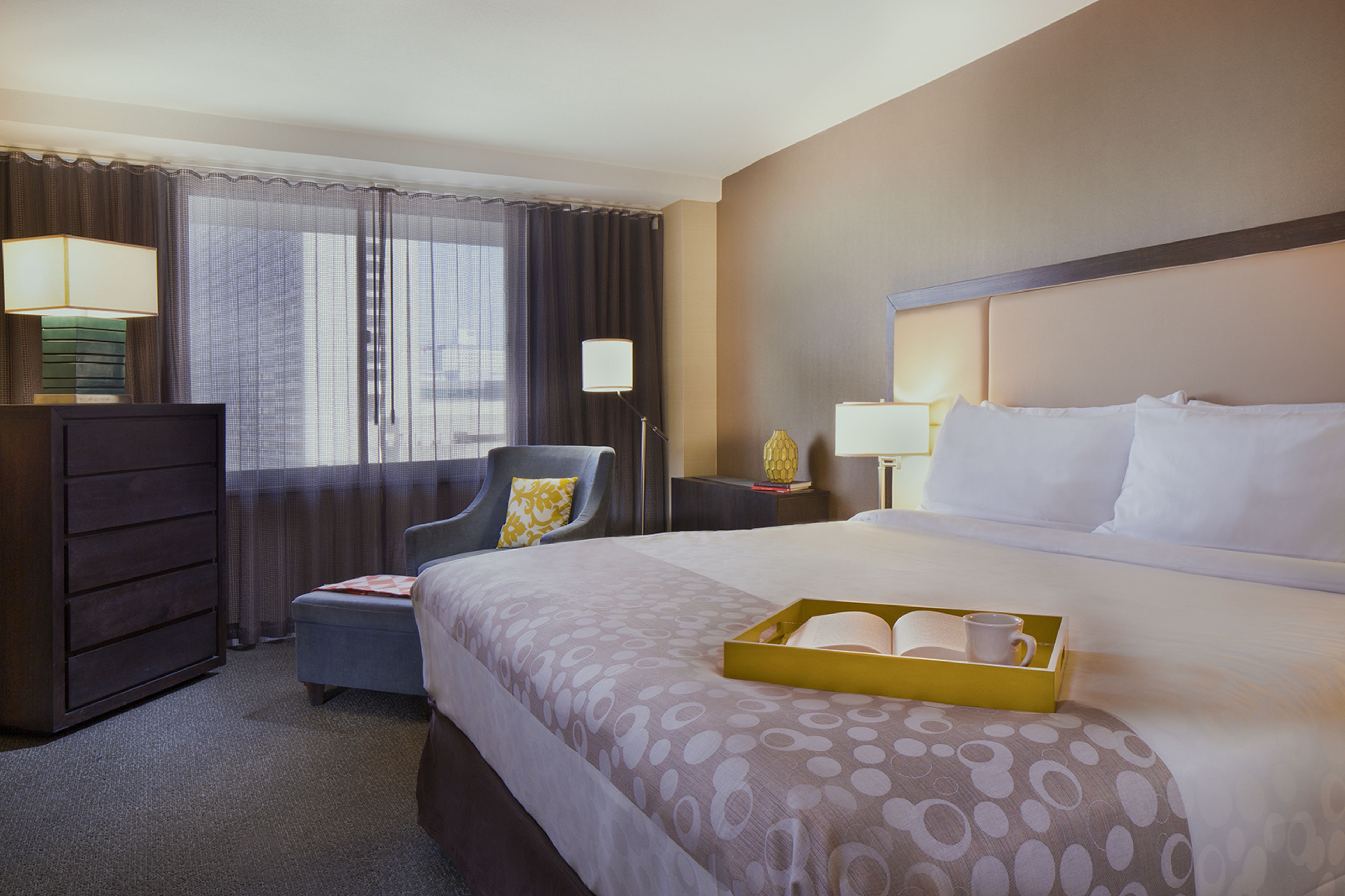 A hotel room with a large bed, a chair, a desk, and a dresser.
