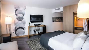A hotel room with a bed, desk, chair, TV, and a large abstract wall art piece.