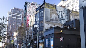 Una strada cittadina con edifici, tra cui un murale e un cartello con su scritto 'DUPLICA'.