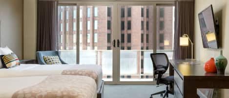 Une chambre d’hôtel avec un grand lit, un bureau avec une chaise, une télévision et une vue sur les bâtiments par la fenêtre.