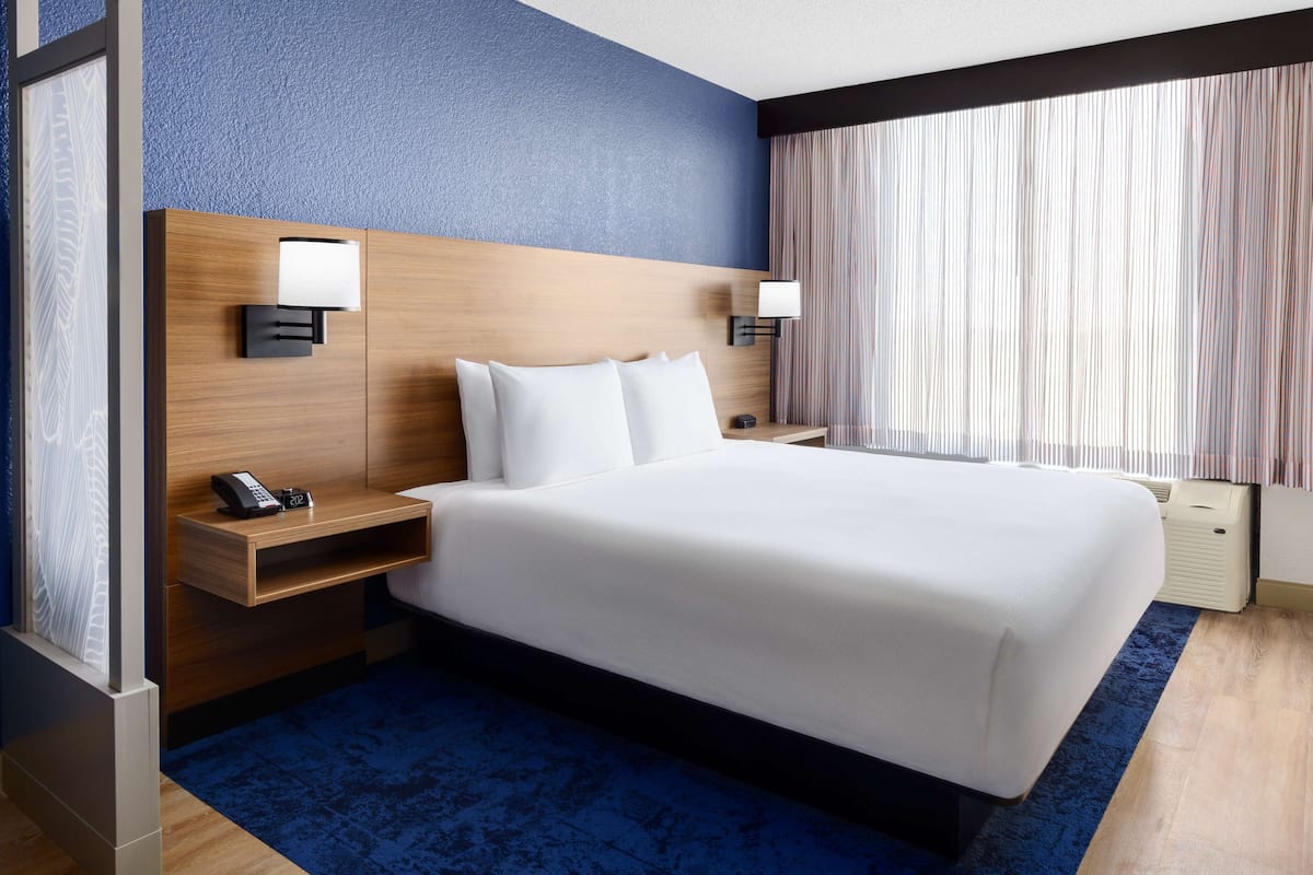 Hotelkamer met een groot bed, een houten hoofdbord, twee nachtkastjes met lampen, een telefoon en een raam met gordijnen.