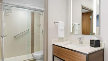 A modern bathroom with a glass shower enclosure, a white toilet, a wooden vanity with a mirror, and a towel rack.