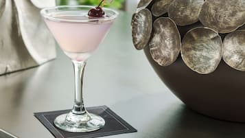 Una copa de martini con una cereza sobre un posavasos negro en una mesa.