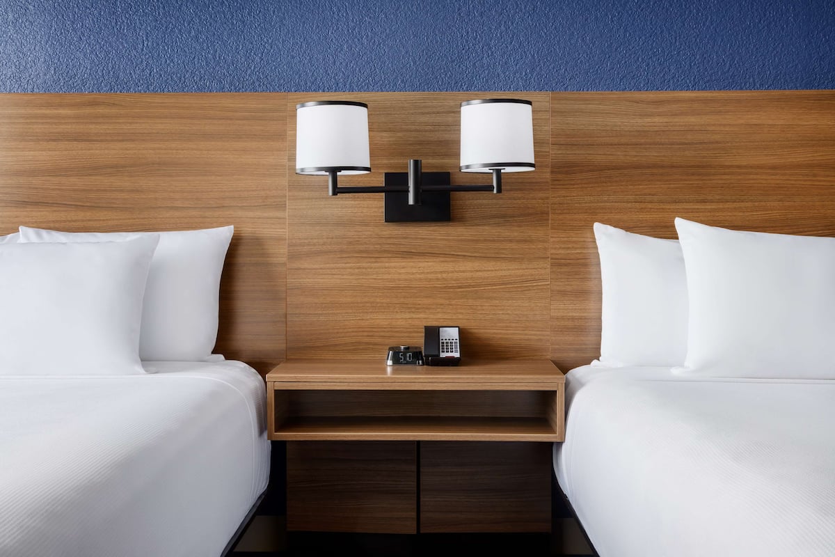 Een hotelkamer met twee bedden, een houten hoofdeinde, een nachtkastje met telefoon en klok, en wandlampen.