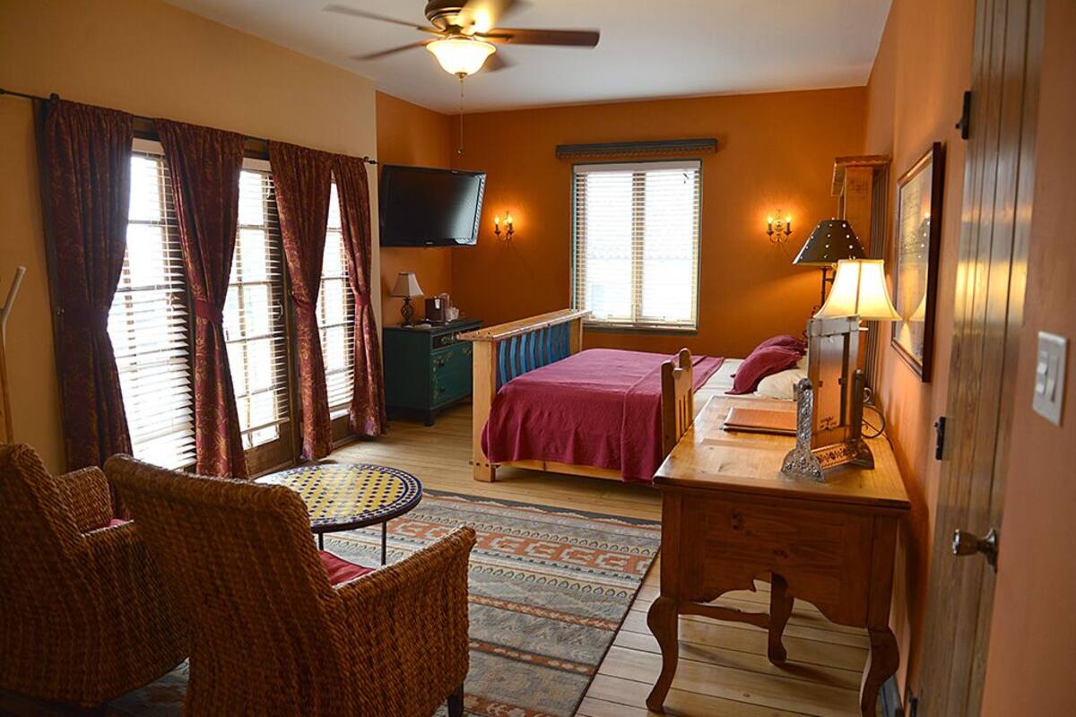 A bedroom with a bed, a desk, a chair, a television, and a ceiling fan.