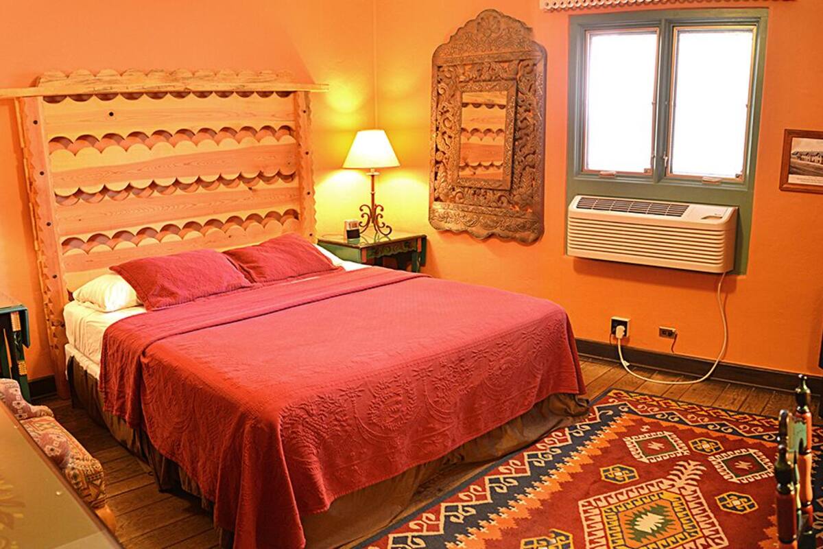 A room with a bed, two bedside tables with lamps, a wall-mounted air conditioner, a television, and a patterned rug.