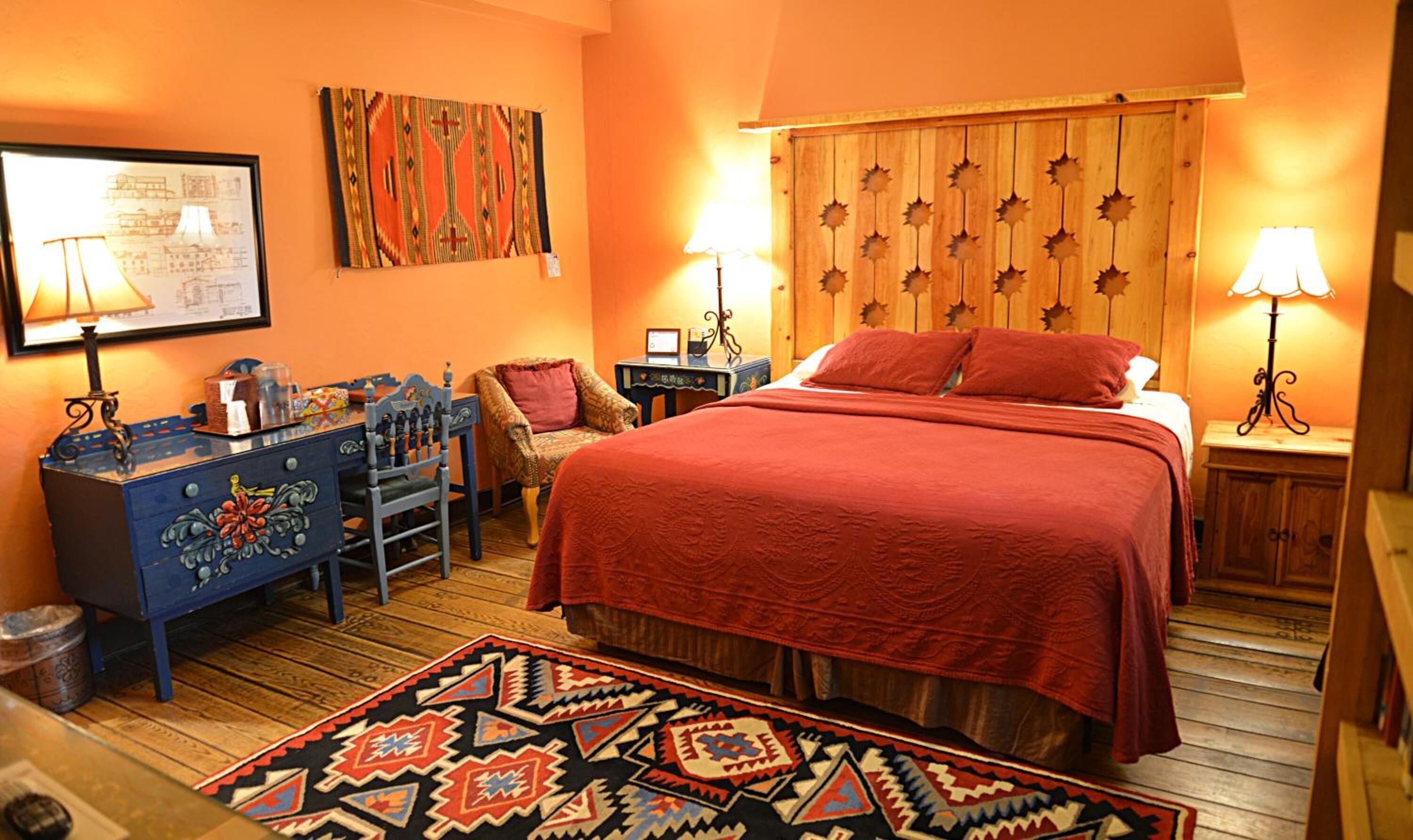 Une chambre confortable avec un grand lit, une tête de lit en bois ornée de motifs en forme d’étoiles, un tapis à motifs et un bureau avec une lampe.