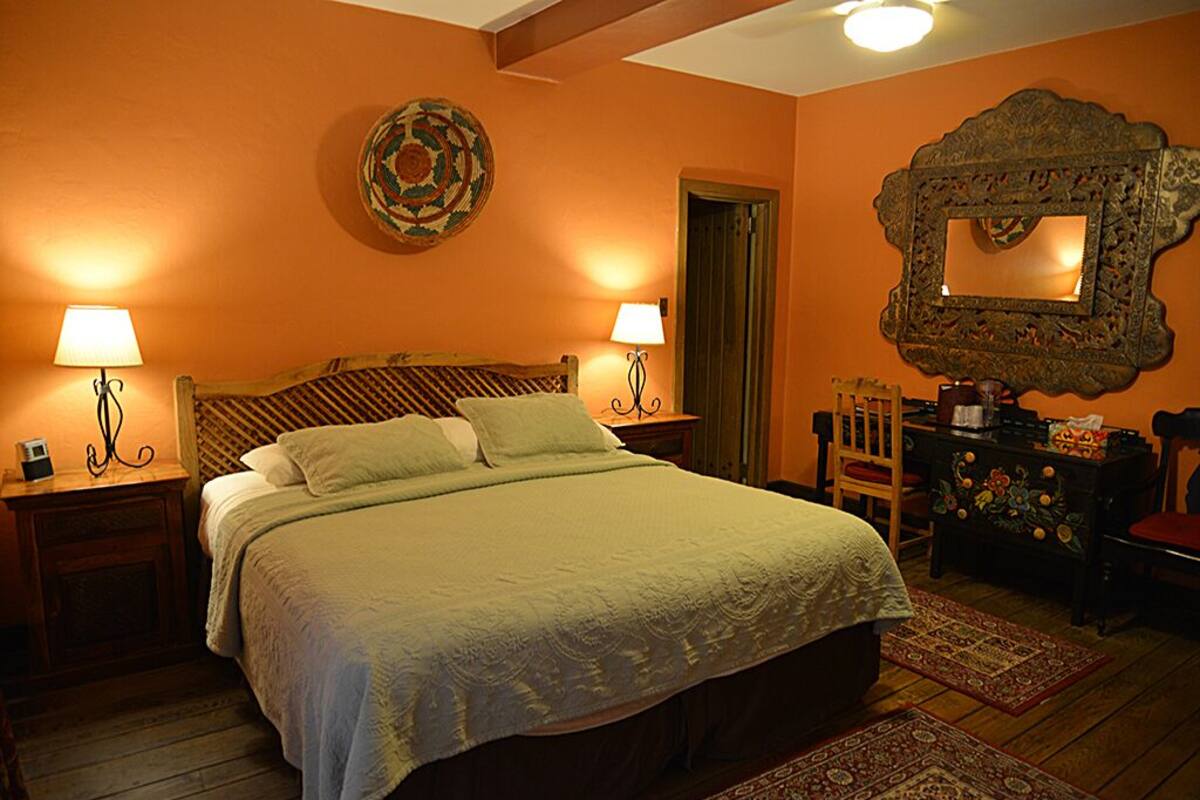 A bedroom with a bed, two bedside tables with lamps, a dresser, a mirror, and a decorative wall hanging.
