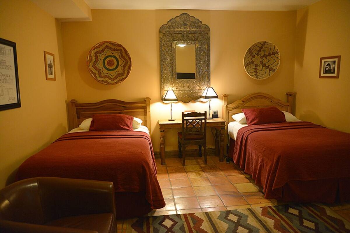 A hotel room with two beds, a desk with lamps, a chair, and decorative plates on the walls.