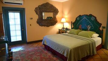 Un dormitorio con cama, mesita de noche, lámpara, espejo y una puerta con persianas.