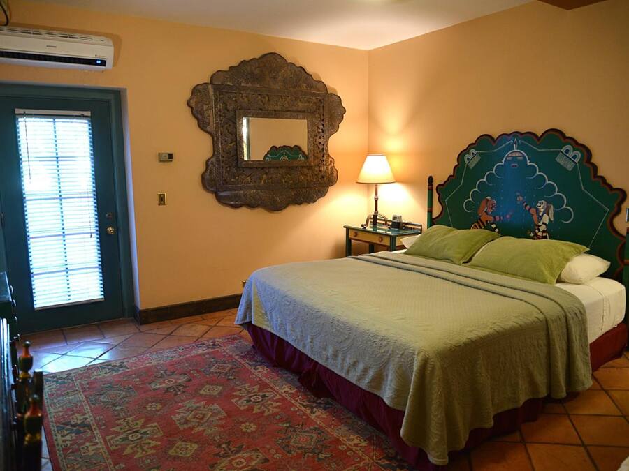 Un dormitorio con cama, mesita de noche, lámpara, espejo y una puerta con persianas.