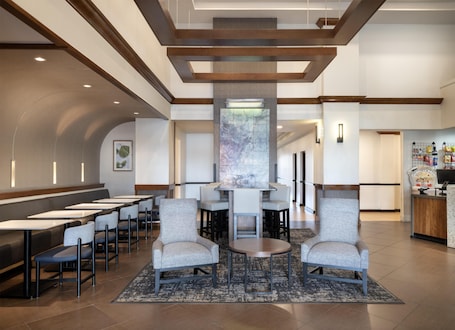 A modern hotel lobby with a central seating area, a reception desk, and a large wall art piece.