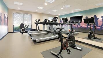A gym with treadmills, stationary bikes, and a mirrored wall.