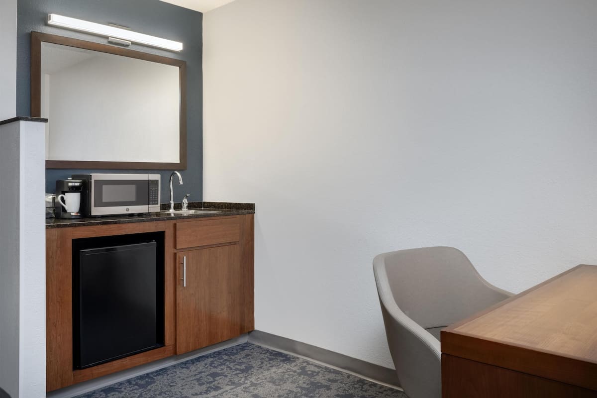 Ein kompaktes Hotelzimmer mit Küchenzeile, einer Mikrowelle, einer Kaffeemaschine, einem Spülbecken und einem Sessel.