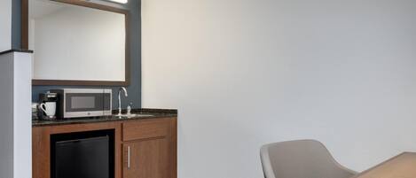 Habitación de hotel compacta con kitchenette, microondas, cafetera, lavabo y una silla.