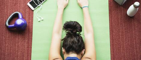 A person lying on a green exercise mat with a smartphone, earphones, a dumbbell, and a water bottle nearby.