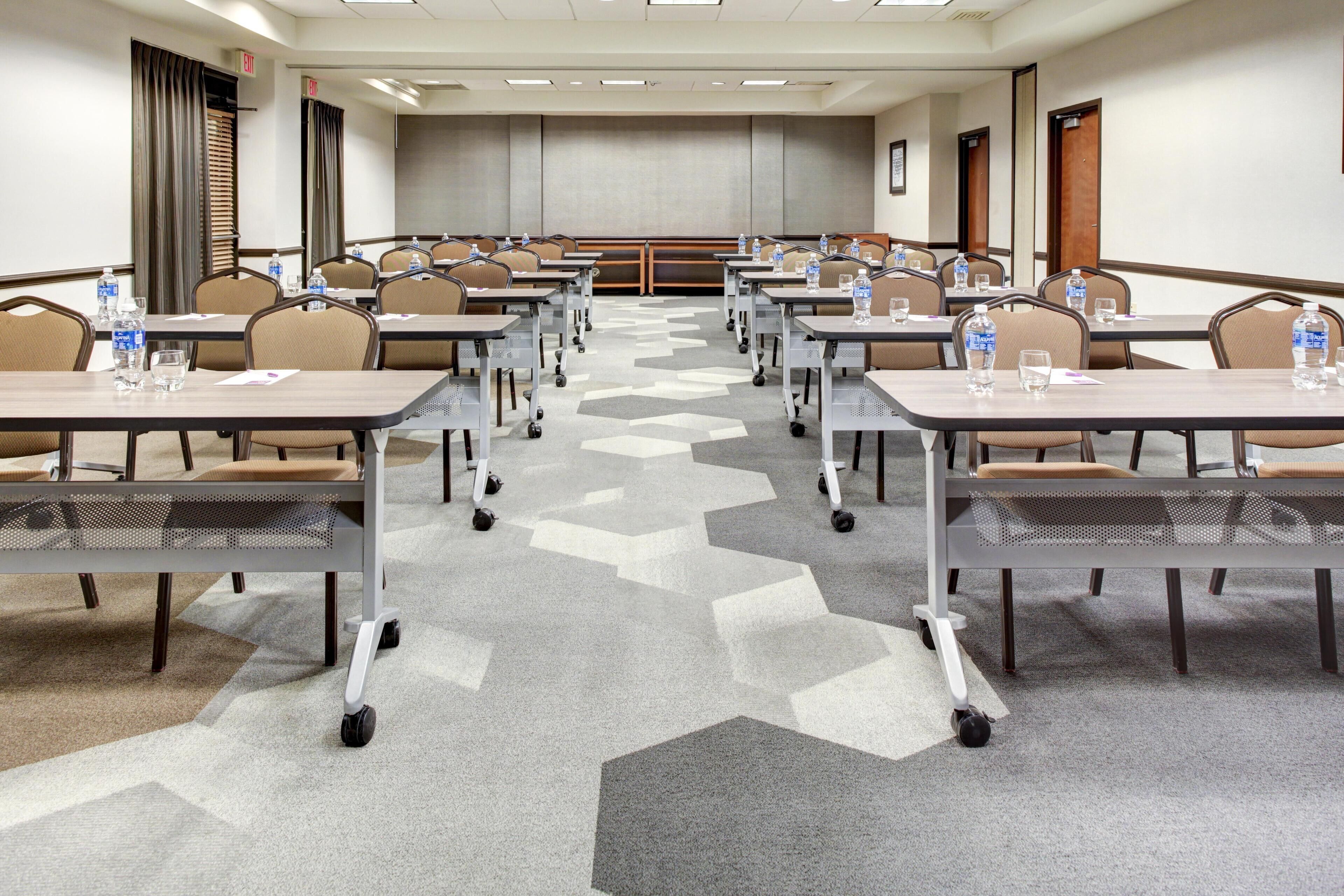 A conference room with multiple tables, chairs, and water bottles.