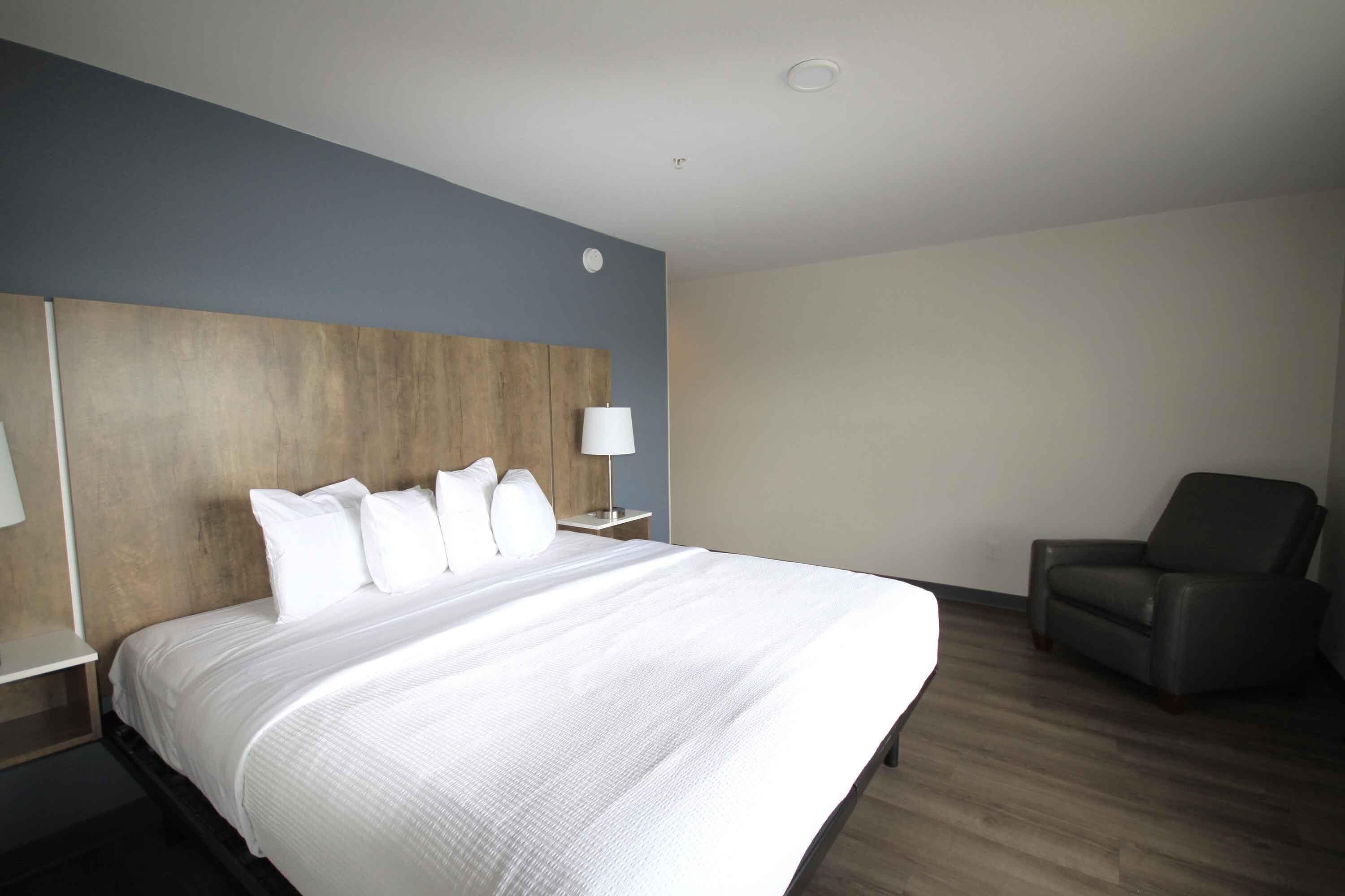 Habitación de hotel con una cama grande, un cabecero de madera, una mesita de noche con una lámpara y un sillón de cuero.